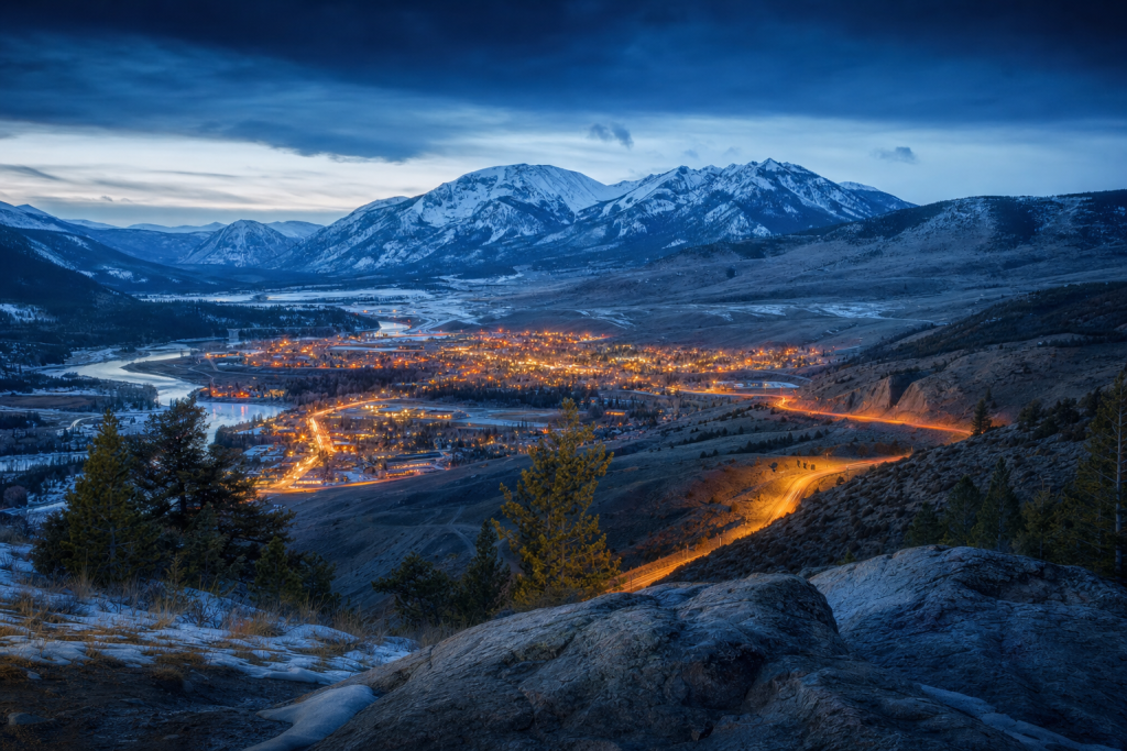 High-vantage view of Yellowstone during blue hour, glowing city lights, subtle motion blur in traffic