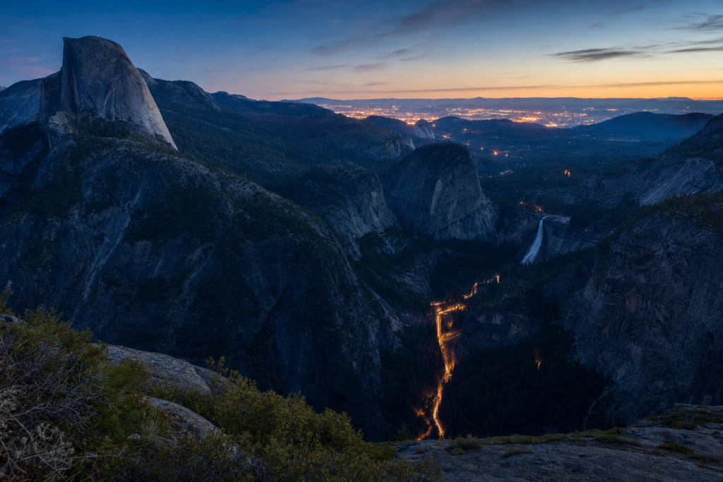 High-vantage view of Yosemite during blue hour, glowing city lights, subtle motion blur in traffic