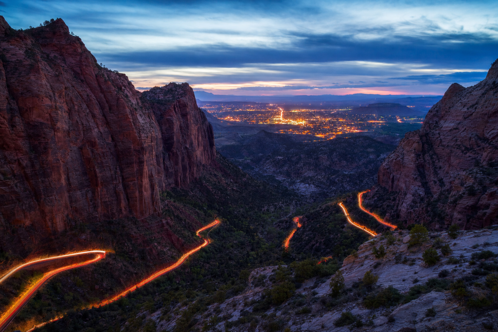 Atmospheric high-vantage view of Zion during blue hour, glowing city lights, subtle motion blur in traffic