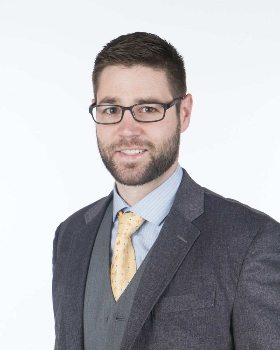 Smiling man wearing glasses and a gray suit against a white studio background, an example corporate headshot