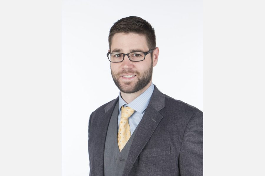Man in glasses and gray suit shown in full against a wide white background, example corporate headshot