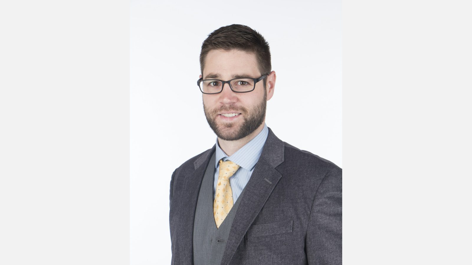 Man in glasses and gray suit shown in full against a wide white background, example corporate headshot