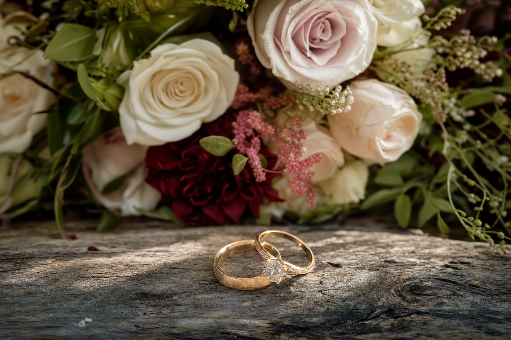 Detail wedding shot: rings and bouquet on textured surface, soft natural light, macro feel, magazine-style composition