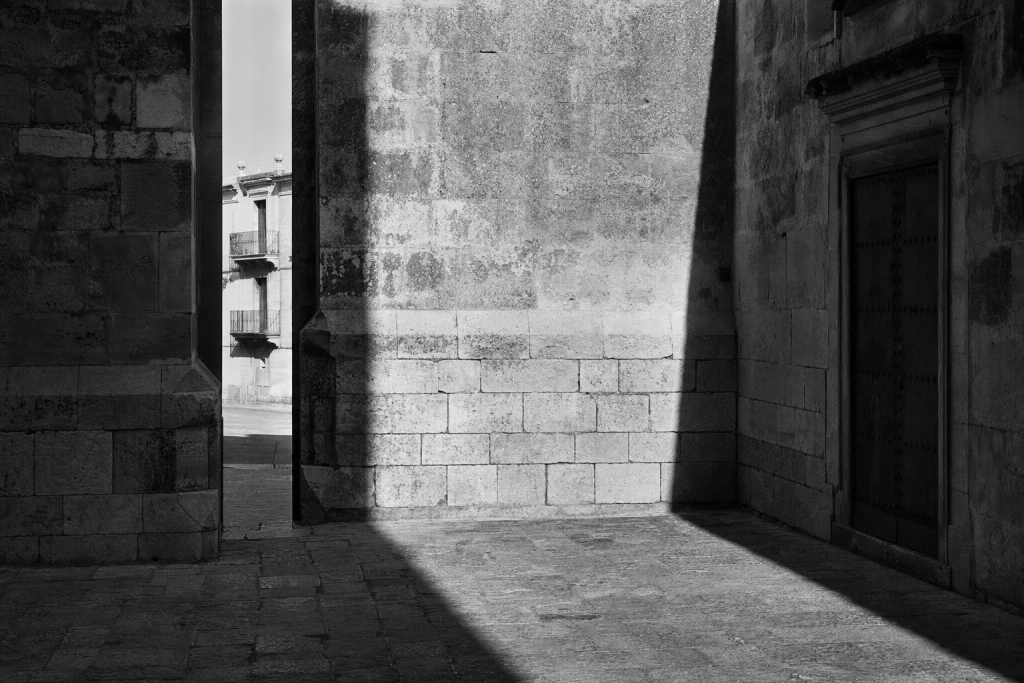 Black-and-white style street composition with strong geometric shadows, high contrast, decisive moment feel