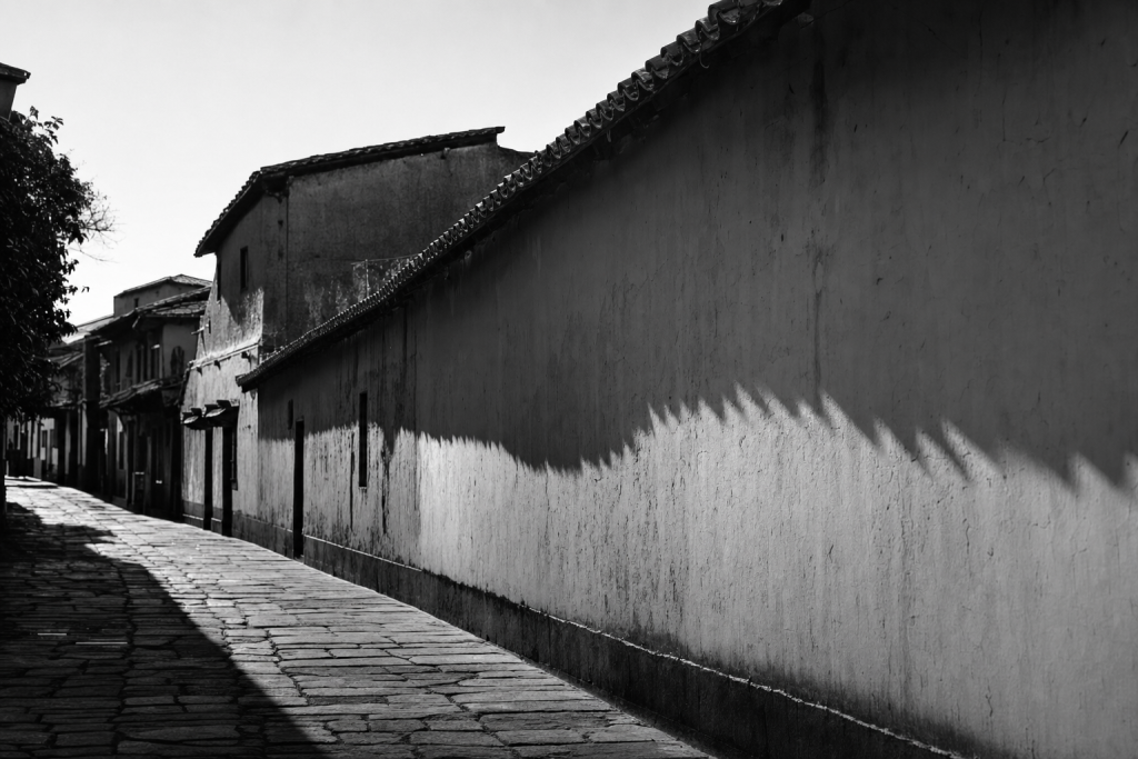 Black-and-white style street composition with strong geometric shadows, high contrast, decisive moment feel