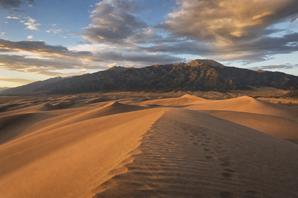 Great Sand Dunes at golden hour, iconic landmarks visible, dramatic warm light