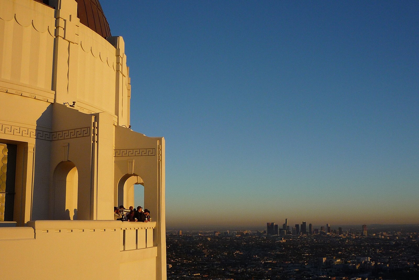 Downtown Los Angeles skyline at twilight viewed from the southern terrace of Griffith Observatory, US Bank Tower and the financial district visible against an orange and blue dusk sky