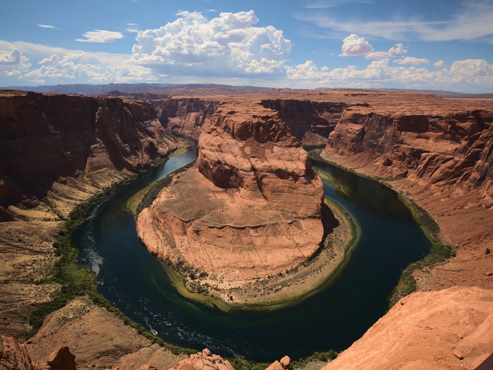 Aerial-perspective view of Horseshoe Bend overlook, Page Arizona, showing the Colorado River making a near-complete horseshoe loop through red Navajo sandstone canyon walls under midday desert light