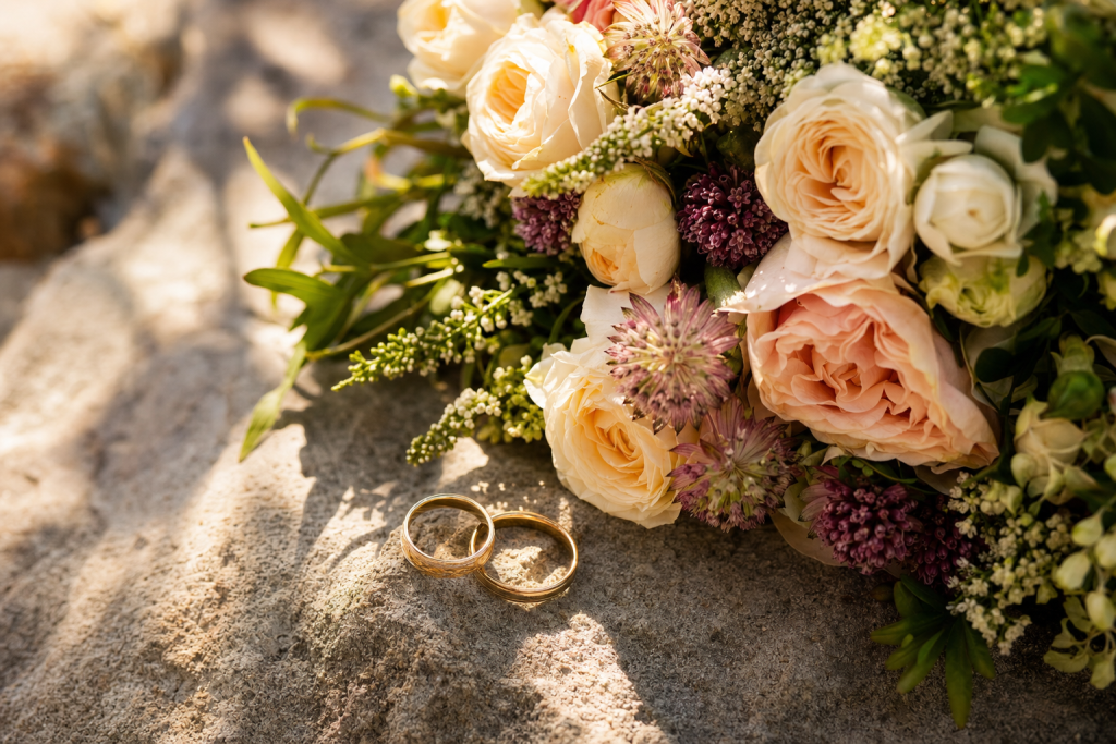 Detail wedding shot: rings and bouquet on textured surface, soft natural light, macro feel, magazine-style composition