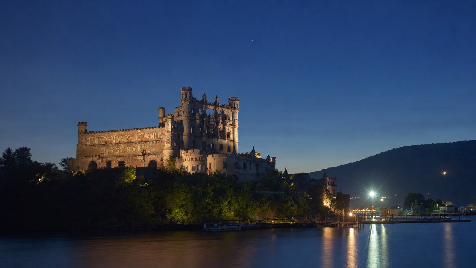 Wide blue-hour view of Bannerman Castle with cobalt sky and warm artificial lighting on the landmark