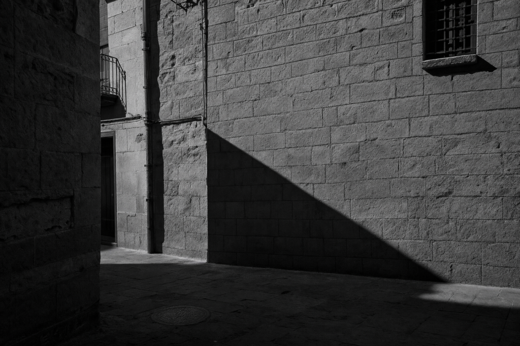 Black-and-white style street composition with strong geometric shadows, high contrast, decisive moment feel