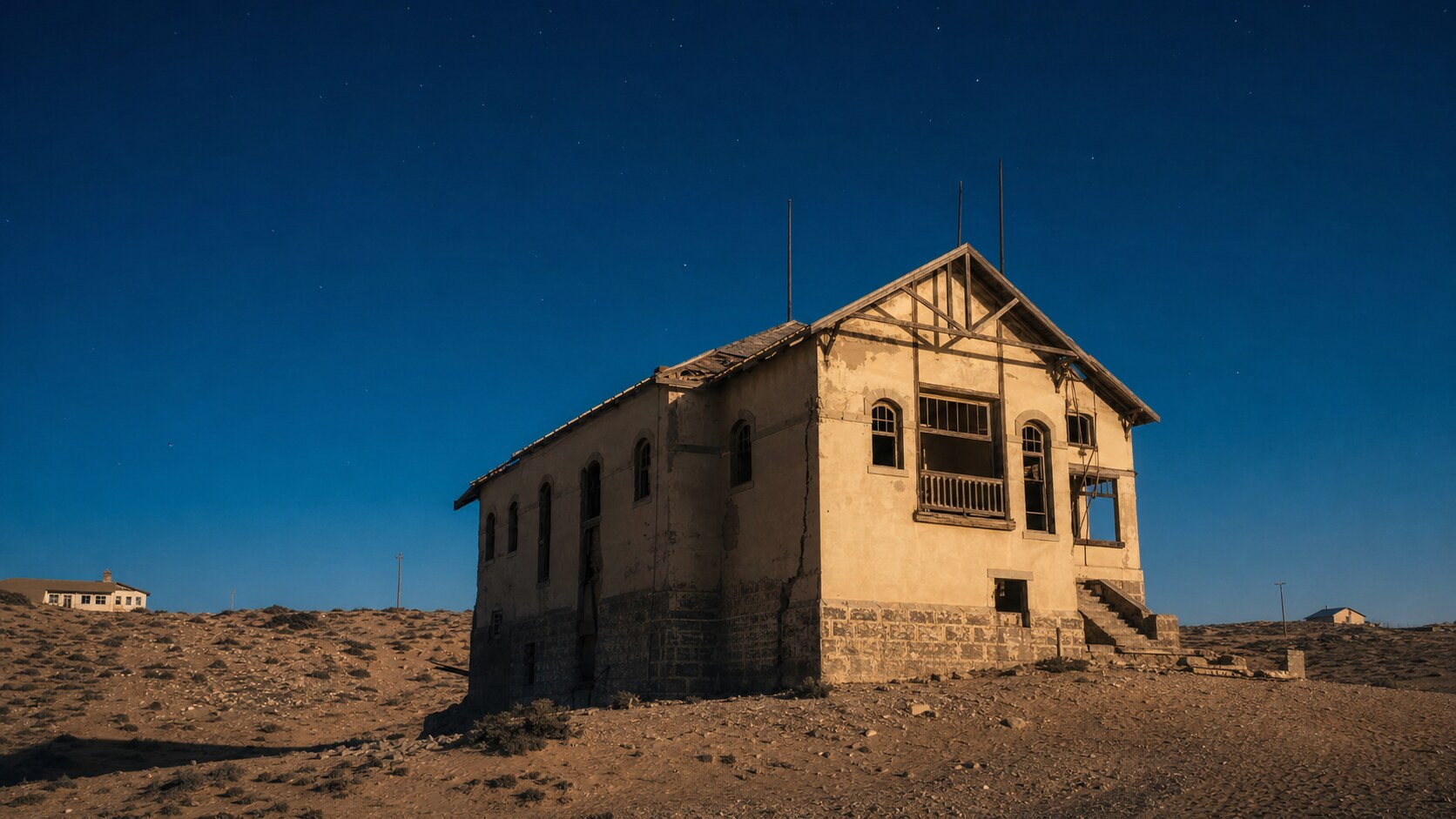Wide blue-hour view of Kolmanskop with cobalt sky and warm artificial lighting on the landmark