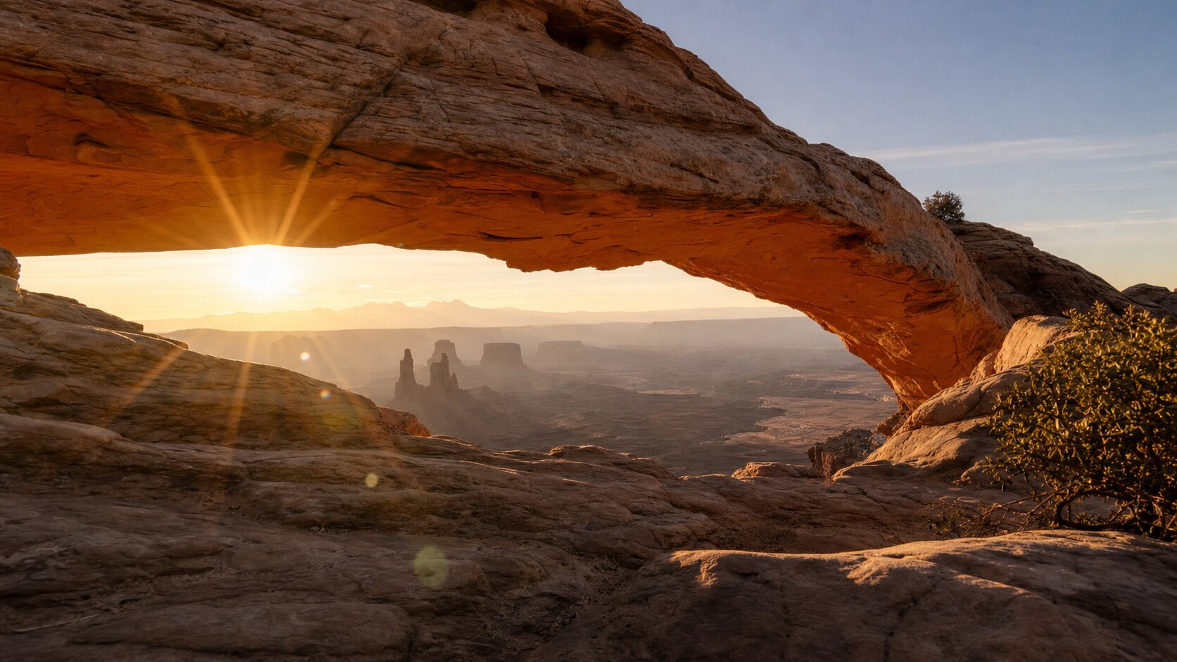 Mesa Arch photographed at golden hour from the most popular hero-shot vantage point, with dramatic side-lighting on the structure