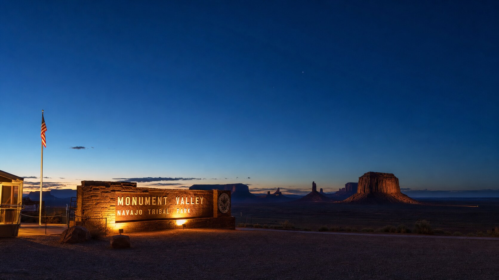 Wide blue-hour view of Monument Valley with cobalt sky and warm artificial lighting on the landmark