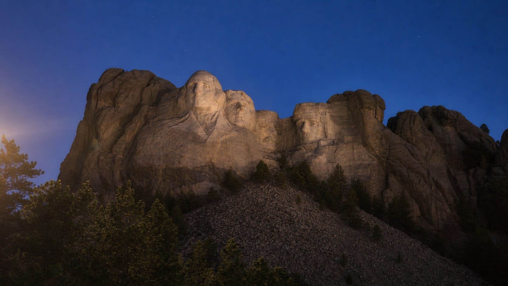 Wide blue-hour view of Mount Rushmore with cobalt sky and warm artificial lighting on the landmark