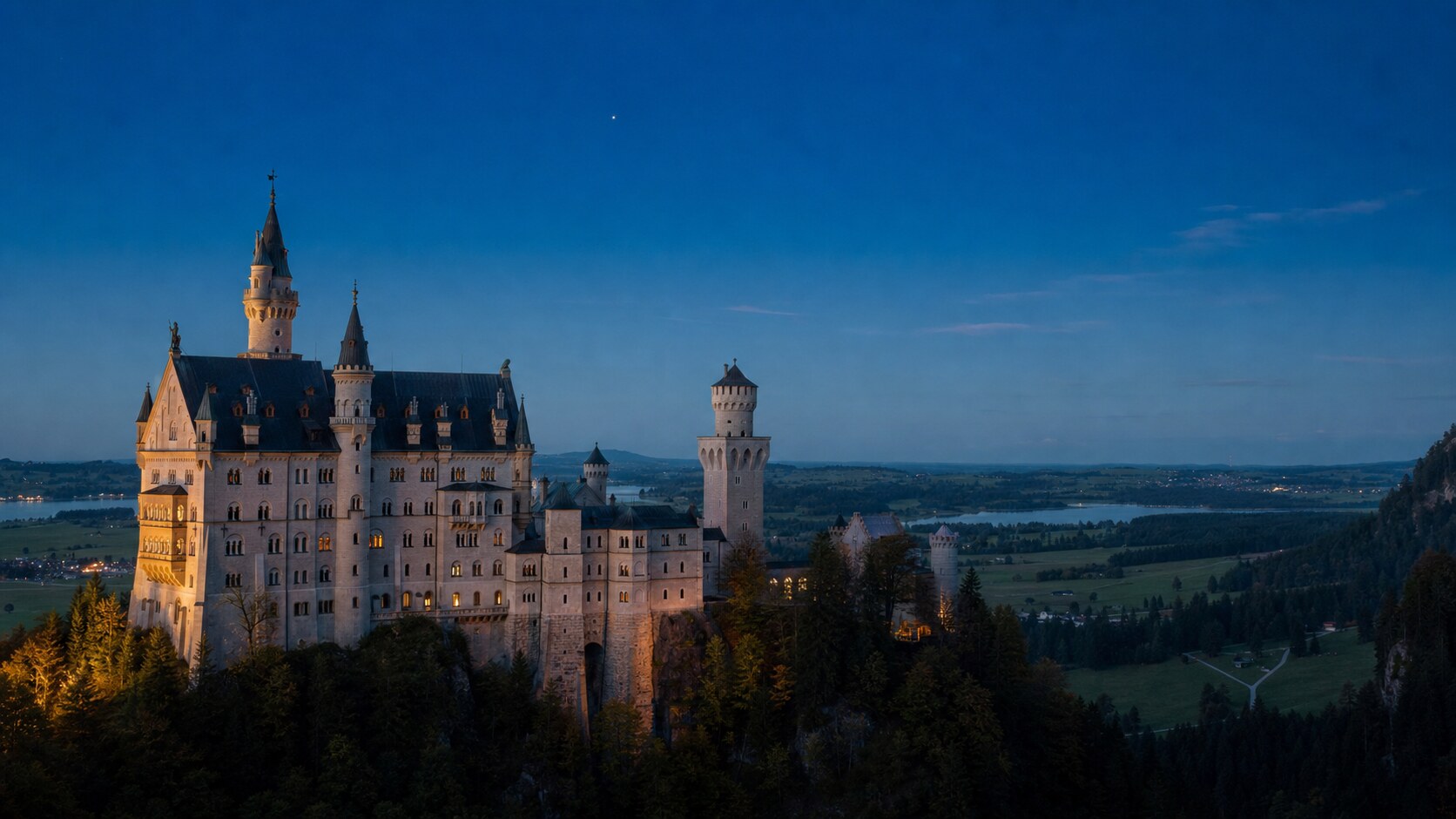 Wide blue-hour view of Neuschwanstein Castle with cobalt sky and warm artificial lighting on the landmark