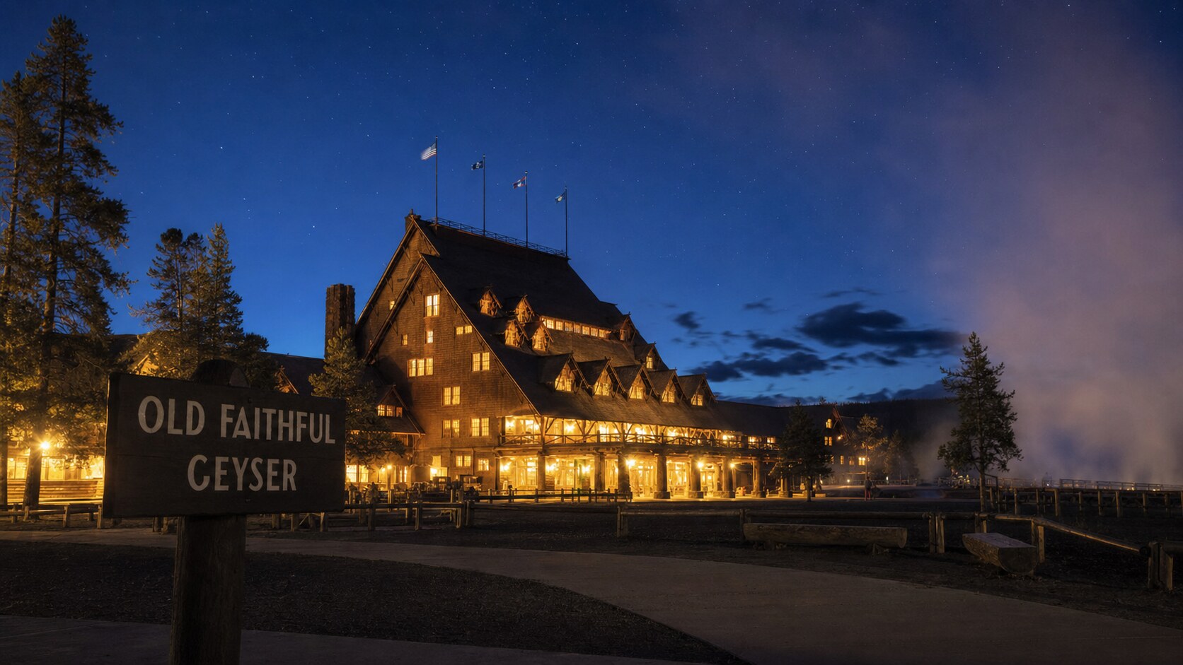 Wide blue-hour view of Old Faithful with cobalt sky and warm artificial lighting on the landmark
