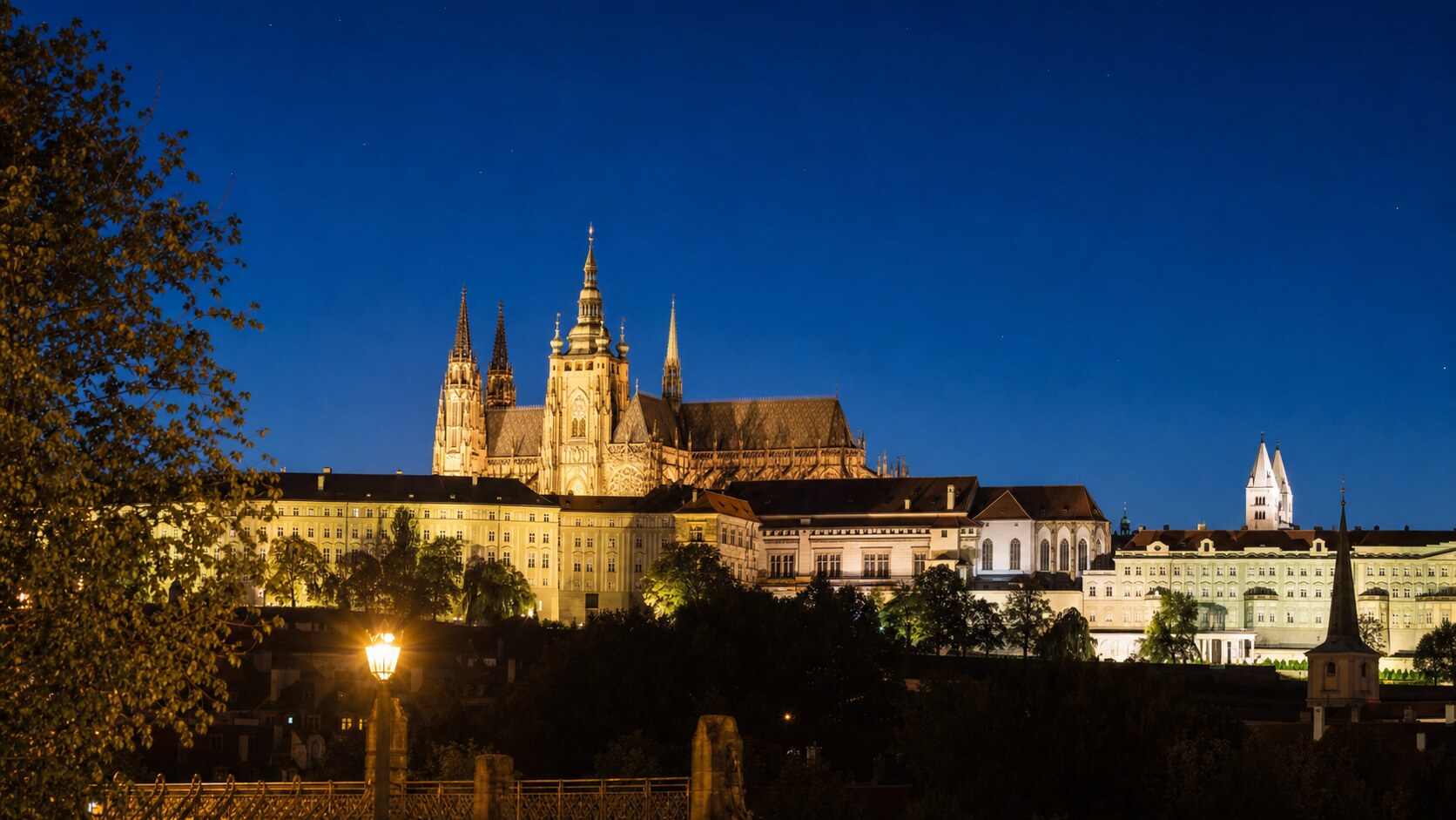 Wide blue-hour view of Prague Castle with cobalt sky and warm artificial lighting on the landmark