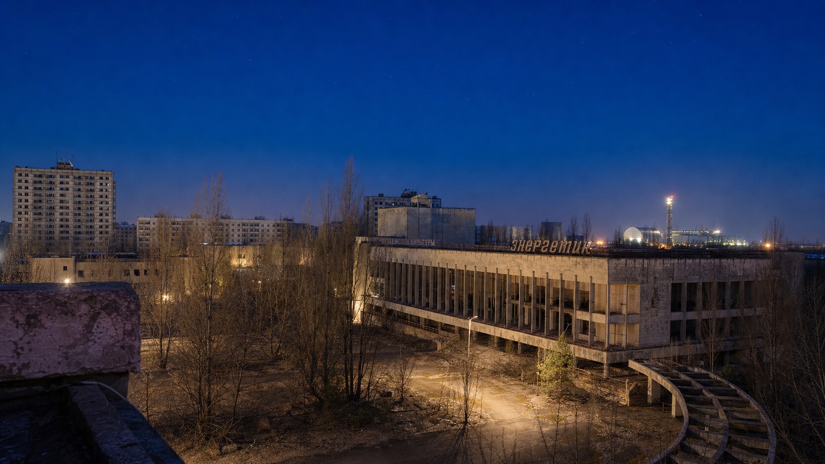 Wide blue-hour view of Pripyat Chernobyl with cobalt sky and warm artificial lighting on the landmark