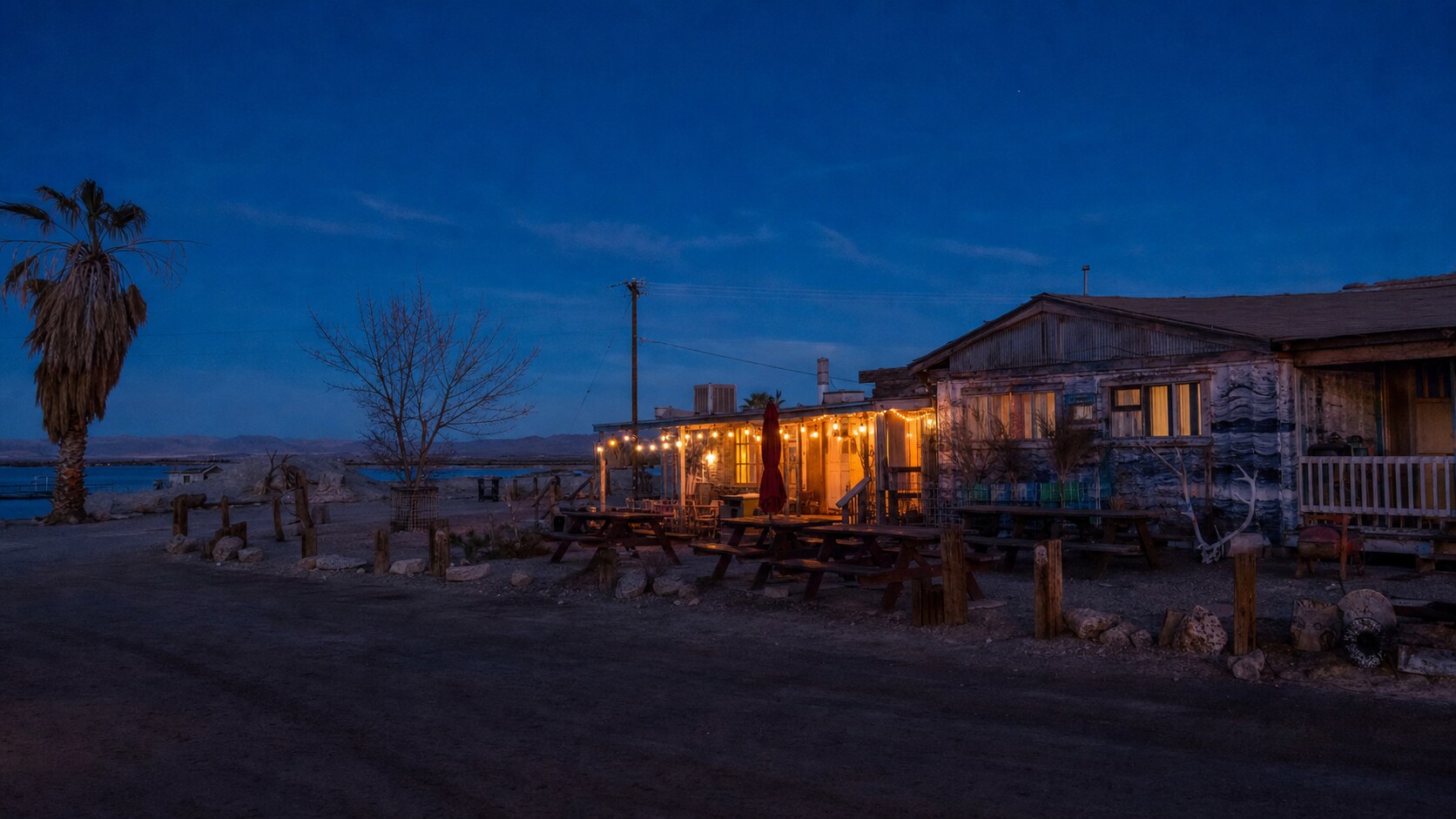 Wide blue-hour view of Salton Sea Bombay Beach with cobalt sky and warm artificial lighting on the landmark