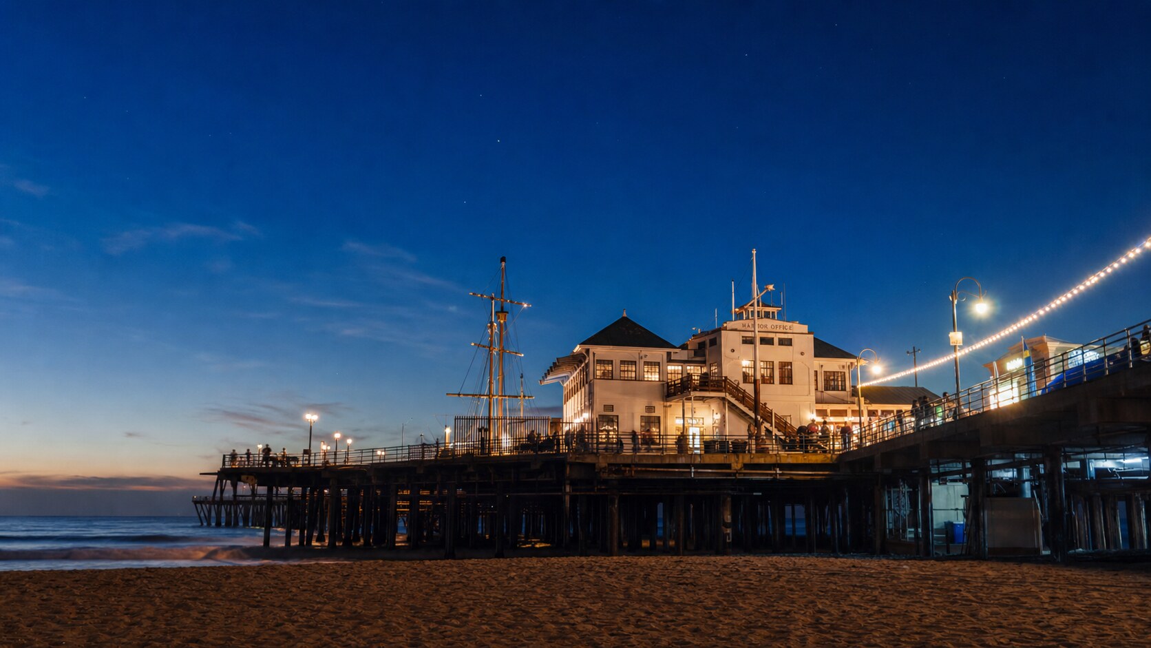Wide blue-hour view of Santa Monica Pier with cobalt sky and warm artificial lighting on the landmark
