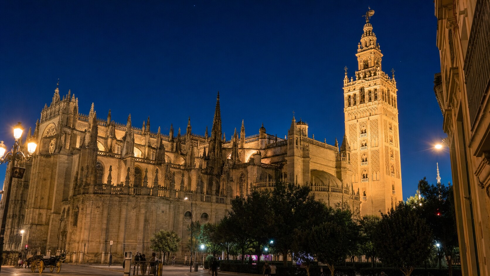 Wide blue-hour view of Seville Cathedral with cobalt sky and warm artificial lighting on the landmark