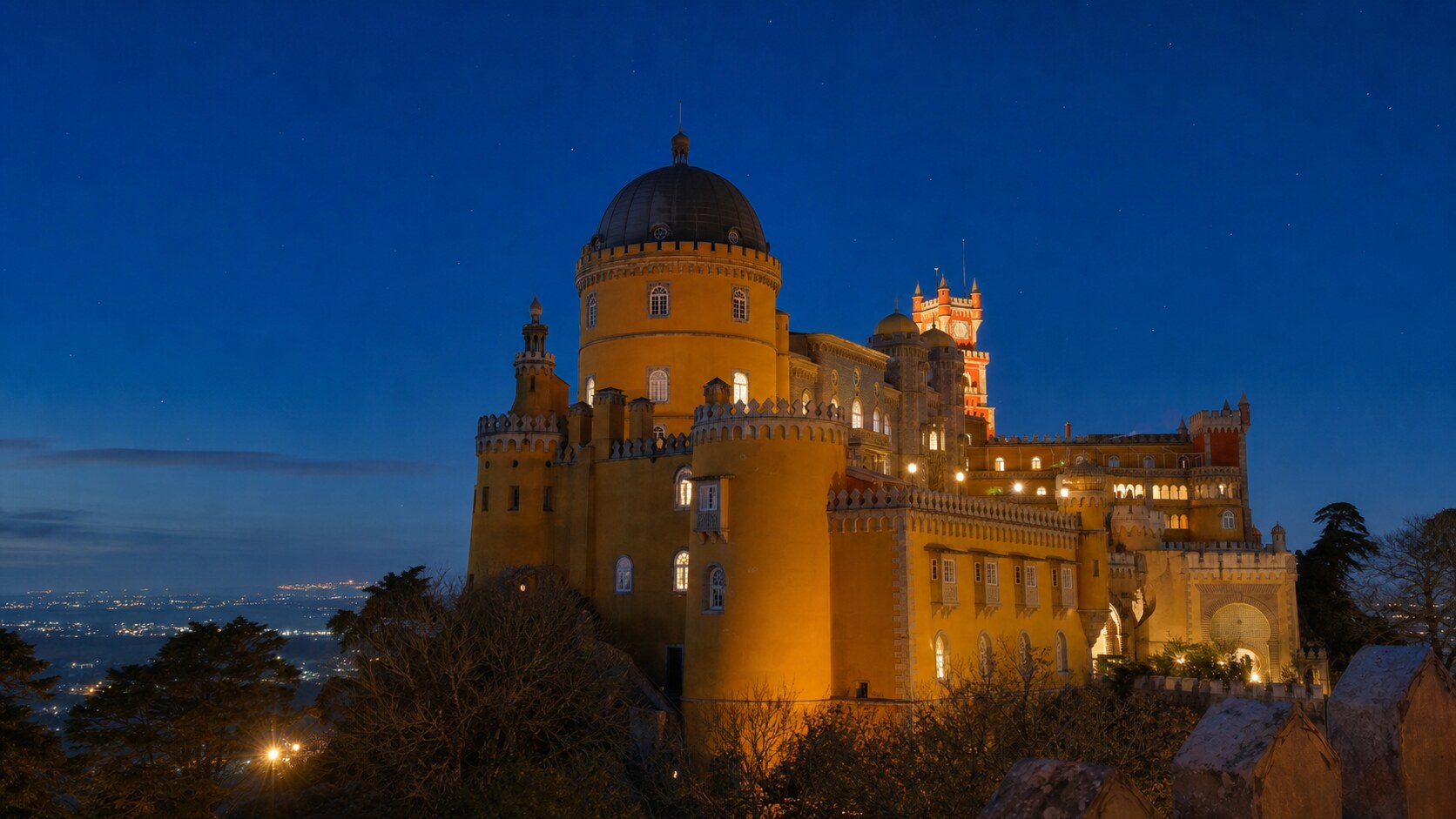 Wide blue-hour view of Sintra Pena Palace with cobalt sky and warm artificial lighting on the landmark