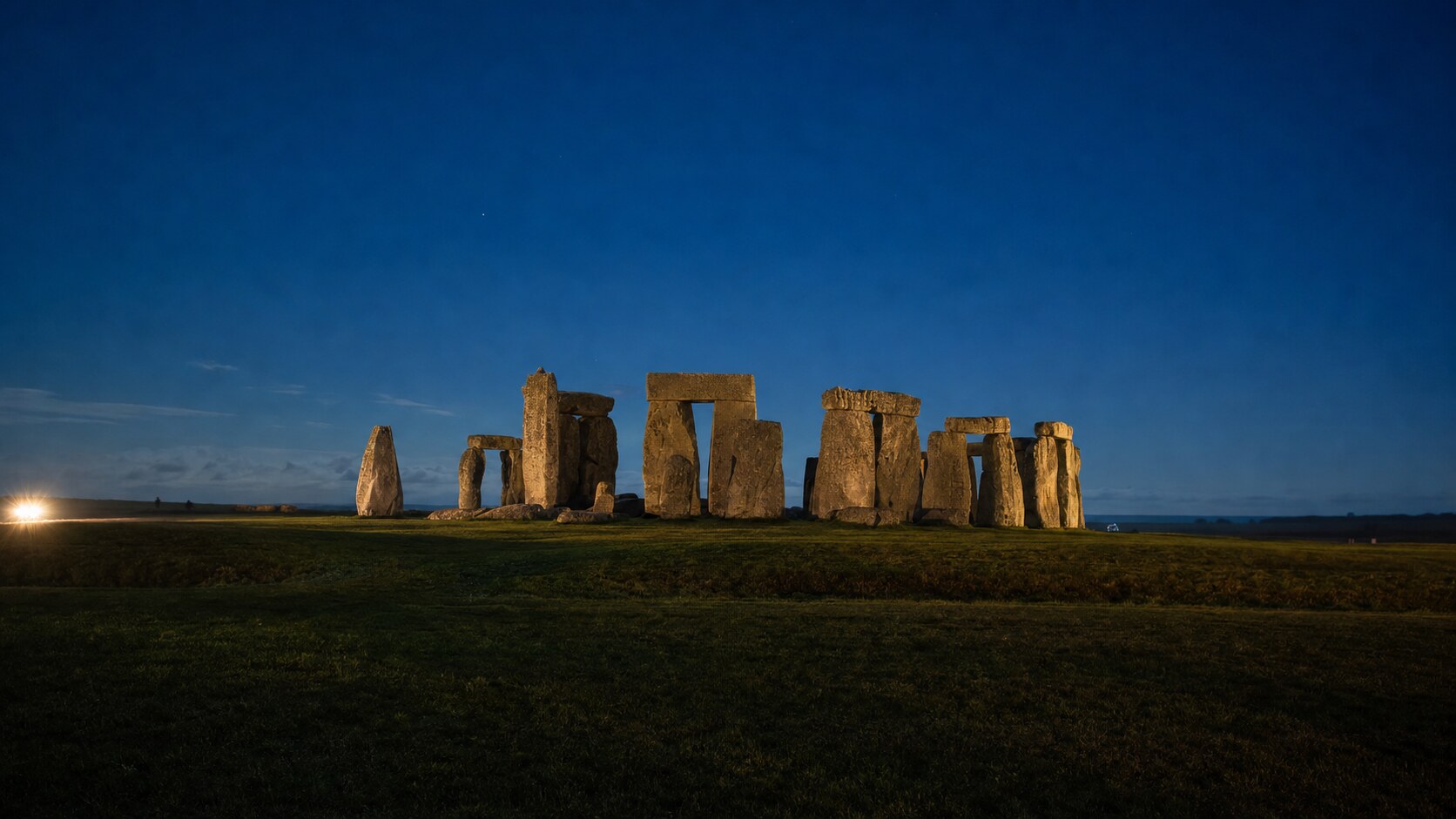 Wide blue-hour view of Stonehenge with cobalt sky and warm artificial lighting on the landmark