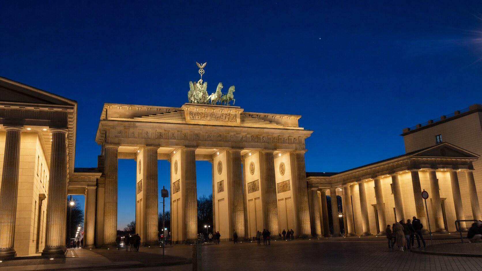 Wide blue-hour view of The Brandenburg Gate with cobalt sky and warm artificial lighting on the landmark