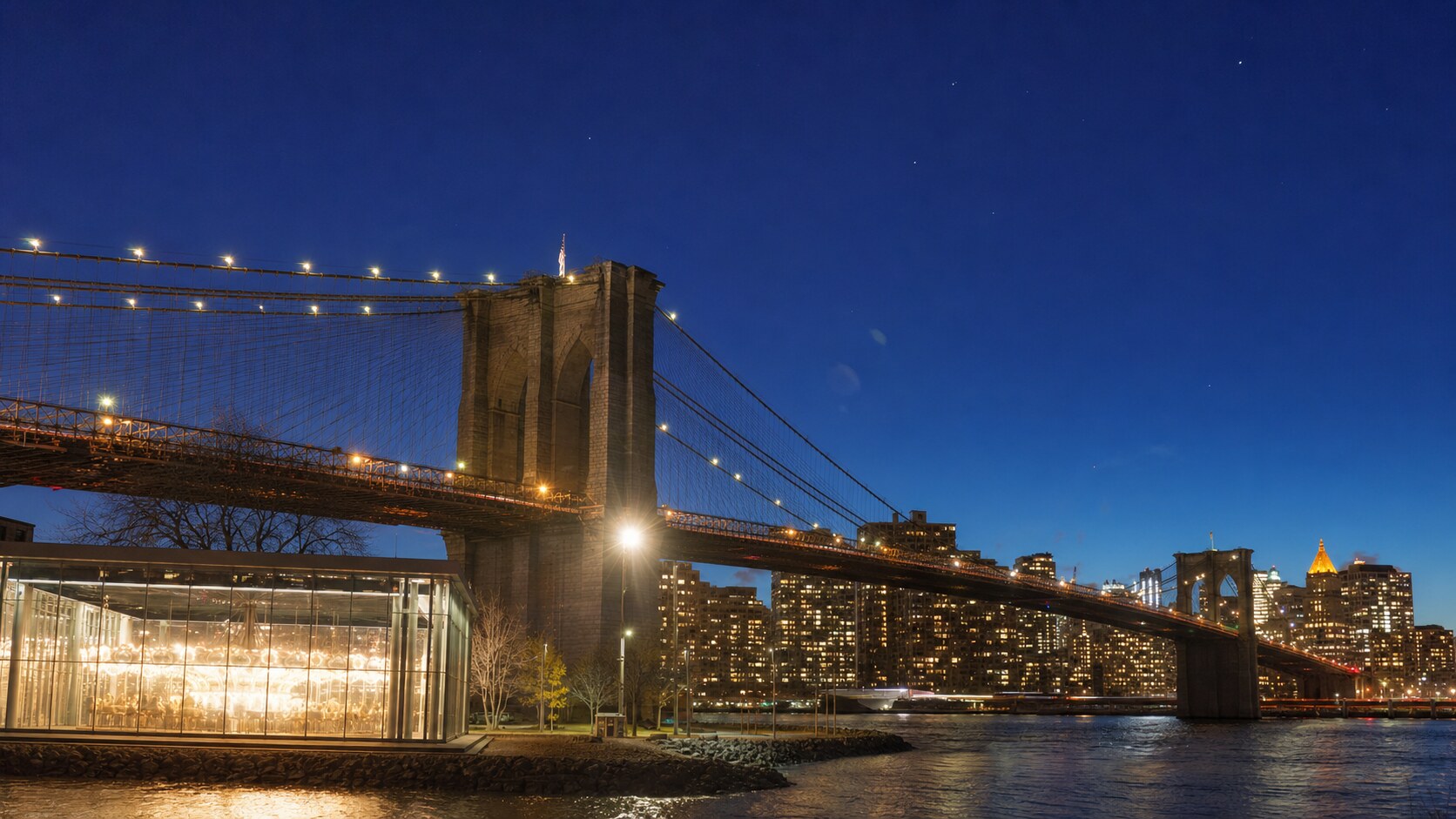 Wide blue-hour view of The Brooklyn Bridge with cobalt sky and warm artificial lighting on the landmark