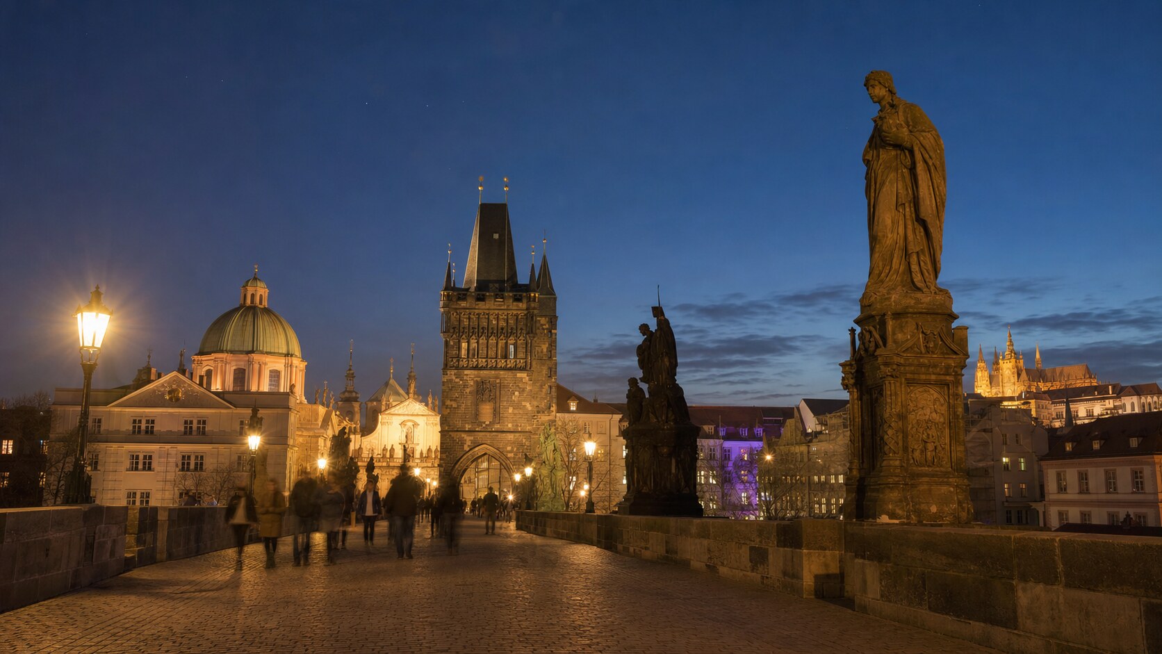 Wide blue-hour view of The Charles Bridge Prague with cobalt sky and warm artificial lighting on the landmark