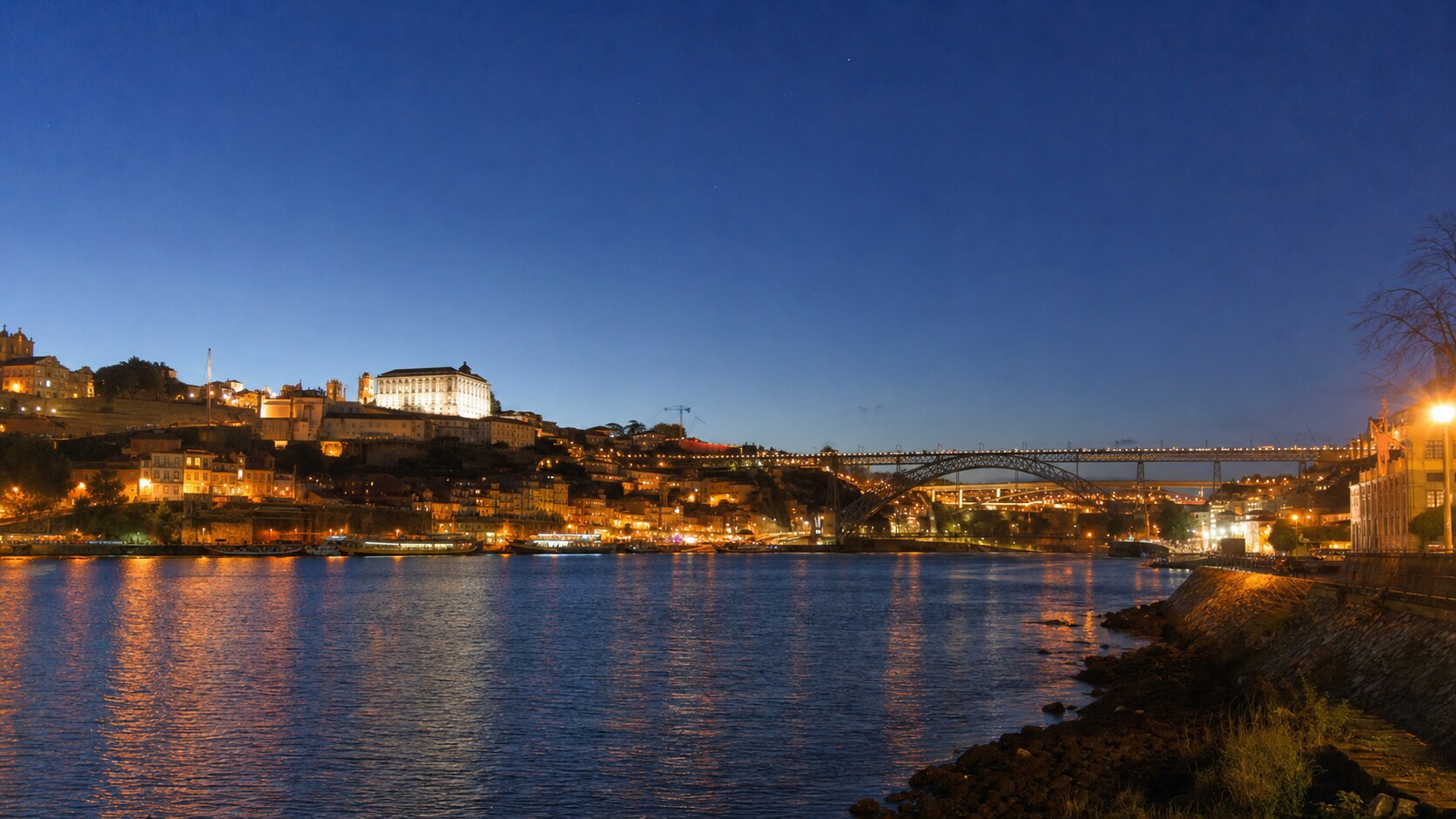 Wide blue-hour view of The Douro River with cobalt sky and warm artificial lighting on the landmark