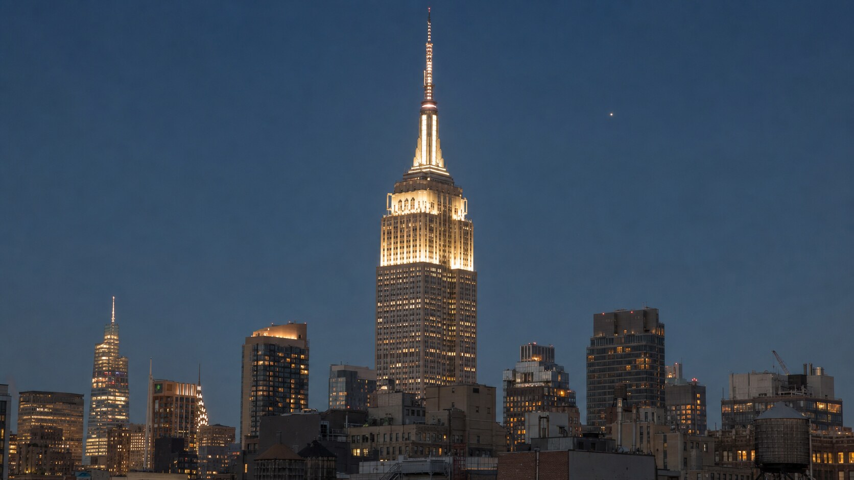 Wide blue-hour view of The Empire State Building with cobalt sky and warm artificial lighting on the landmark