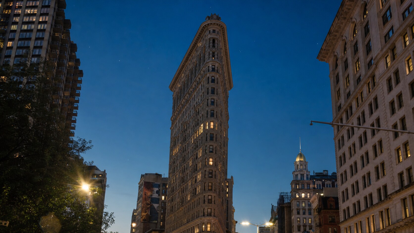 Wide blue-hour view of The Flatiron Building with cobalt sky and warm artificial lighting on the landmark