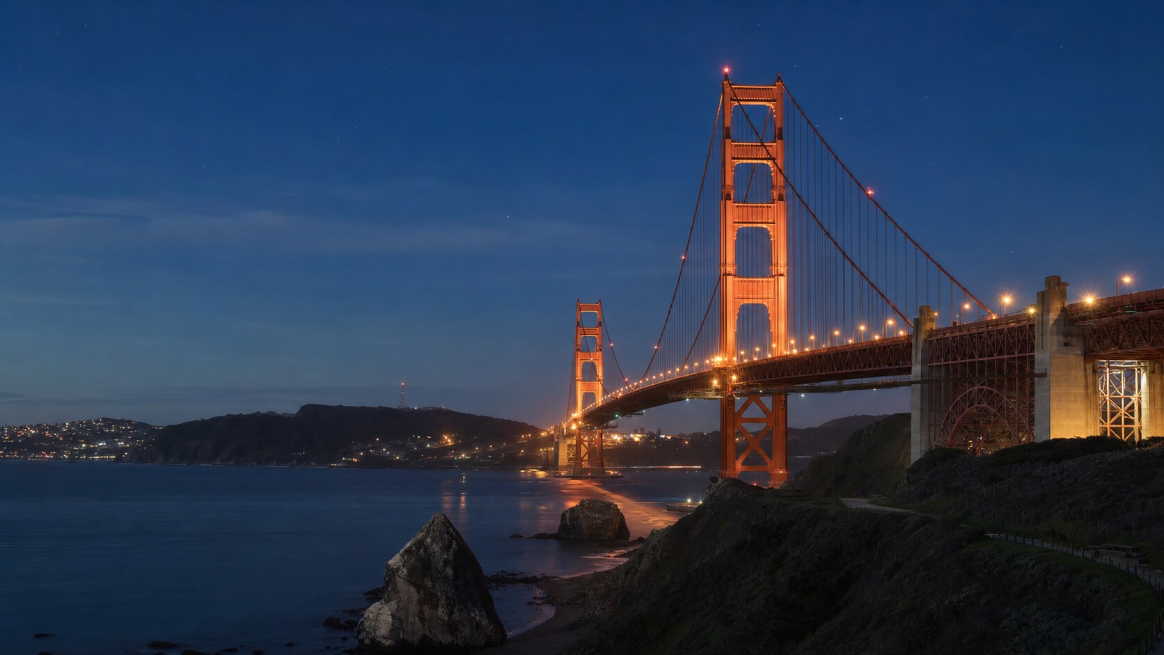 Wide blue-hour view of The Golden Gate Bridge with cobalt sky and warm artificial lighting on the landmark