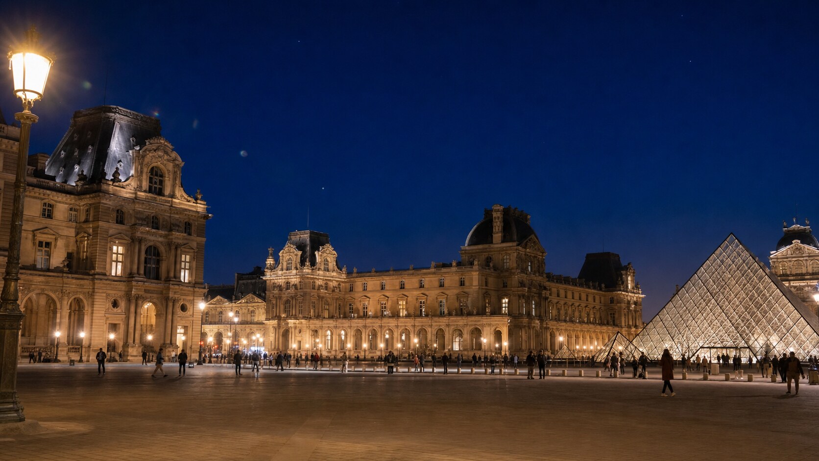 Wide blue-hour view of The Louvre with cobalt sky and warm artificial lighting on the landmark