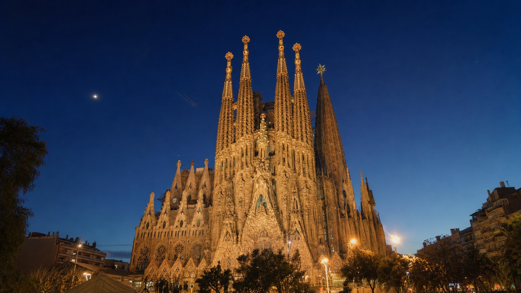 Wide blue-hour view of The Sagrada Familia with cobalt sky and warm artificial lighting on the landmark