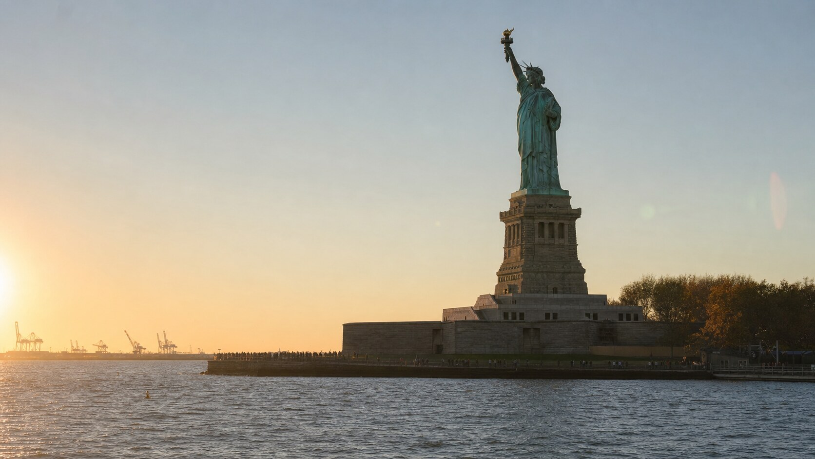 The Statue Of Liberty photographed at golden hour from the most popular hero-shot vantage point, with dramatic side-lighting on the structure