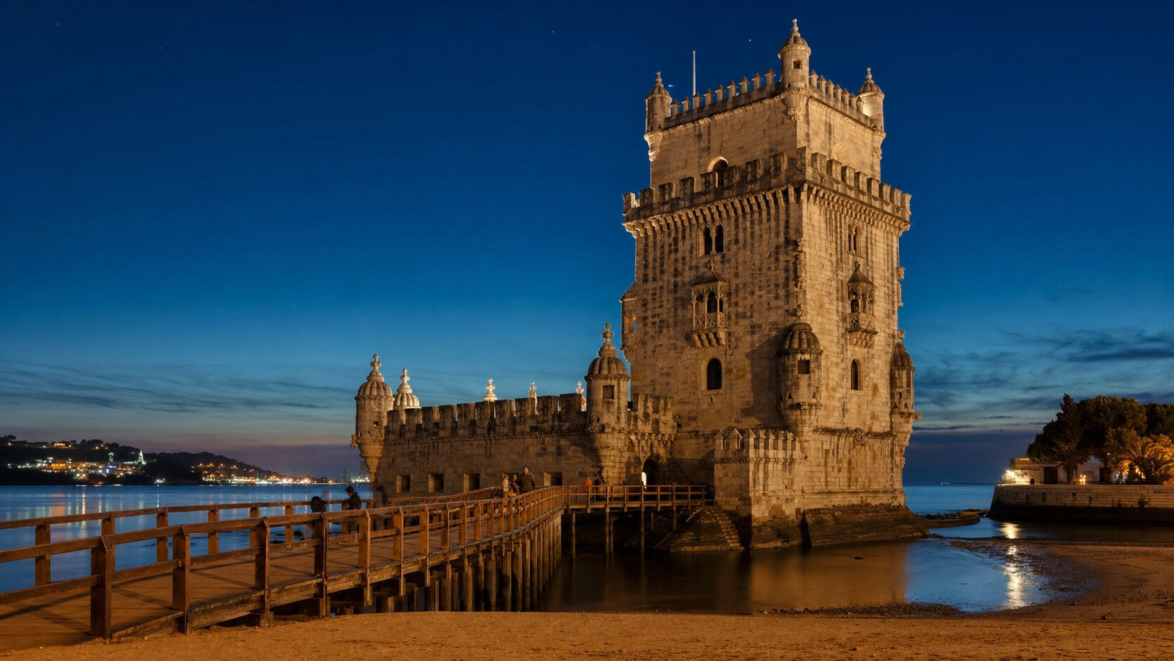 Wide blue-hour view of The Tower Of Belem with cobalt sky and warm artificial lighting on the landmark