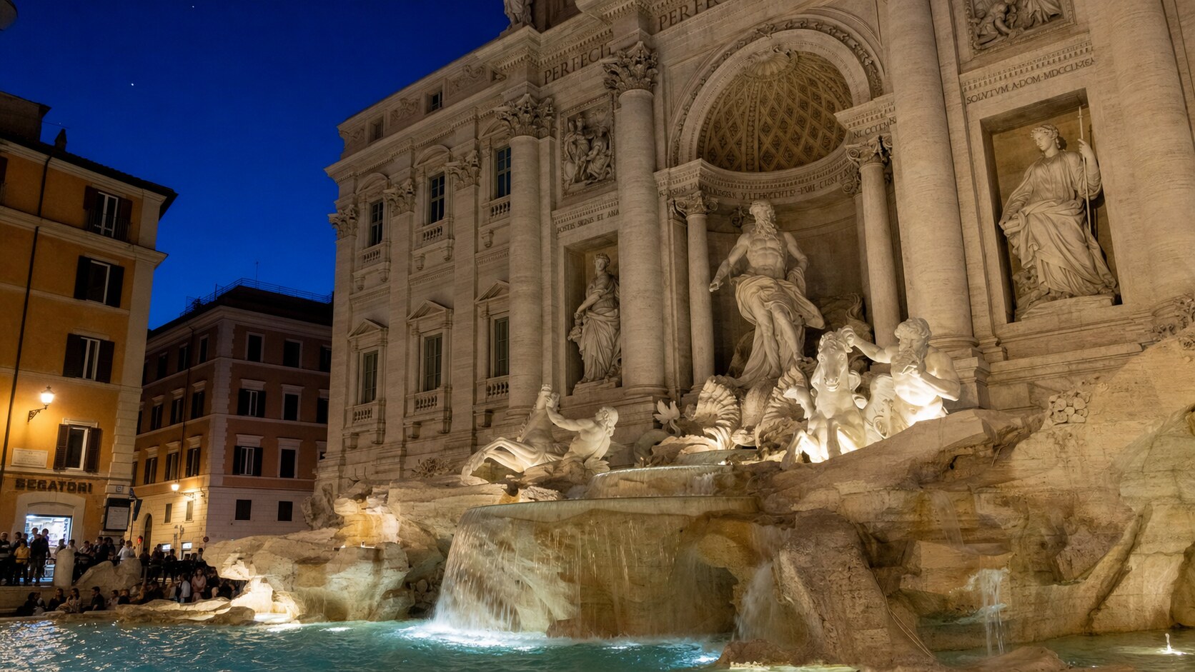 Wide blue-hour view of The Trevi Fountain Rome with cobalt sky and warm artificial lighting on the landmark