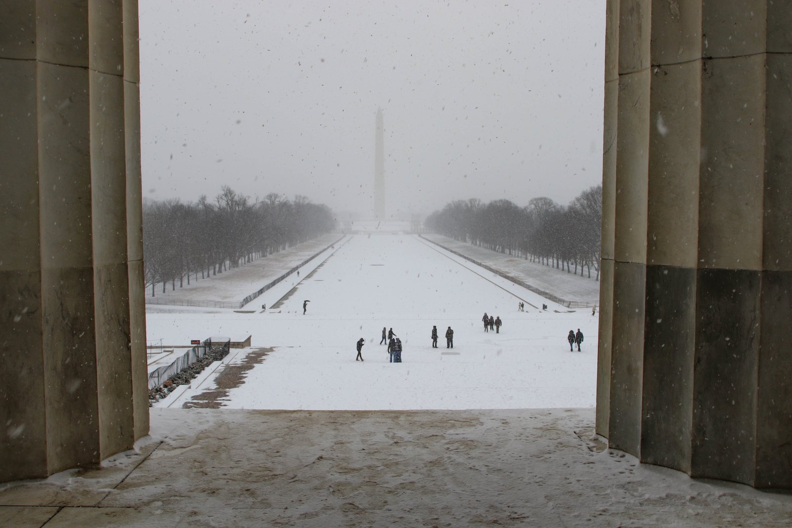 View through Lincoln Memorial pillars looking east across snow-covered Reflecting Pool toward the Washington Monument, National Mall, Washington DC