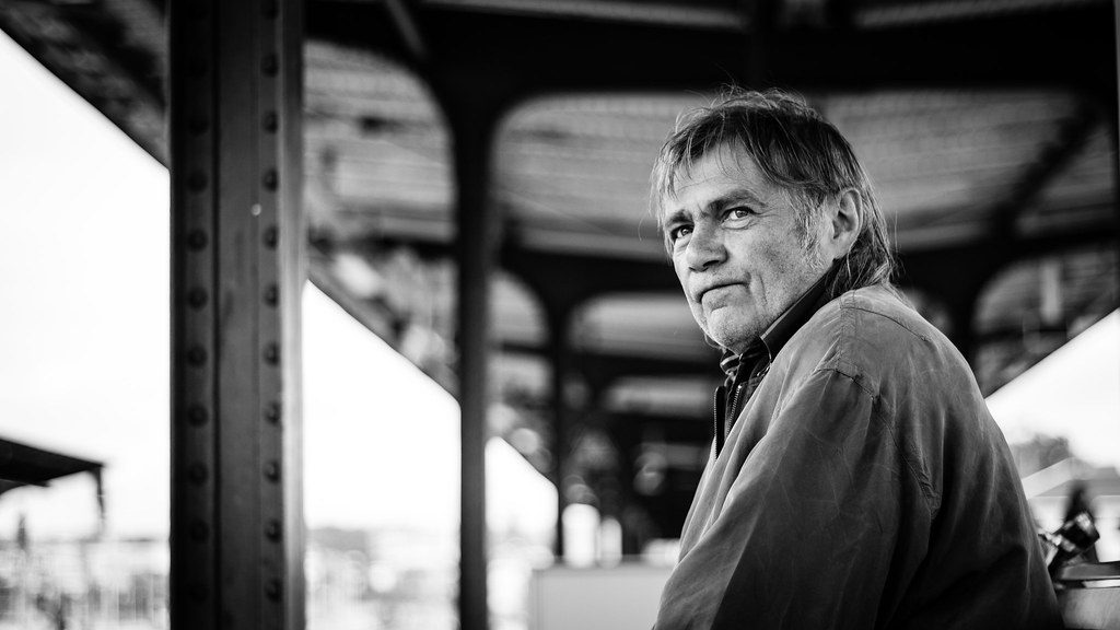 Street photography foreground framing using bridge railings to capture a distant street performer.