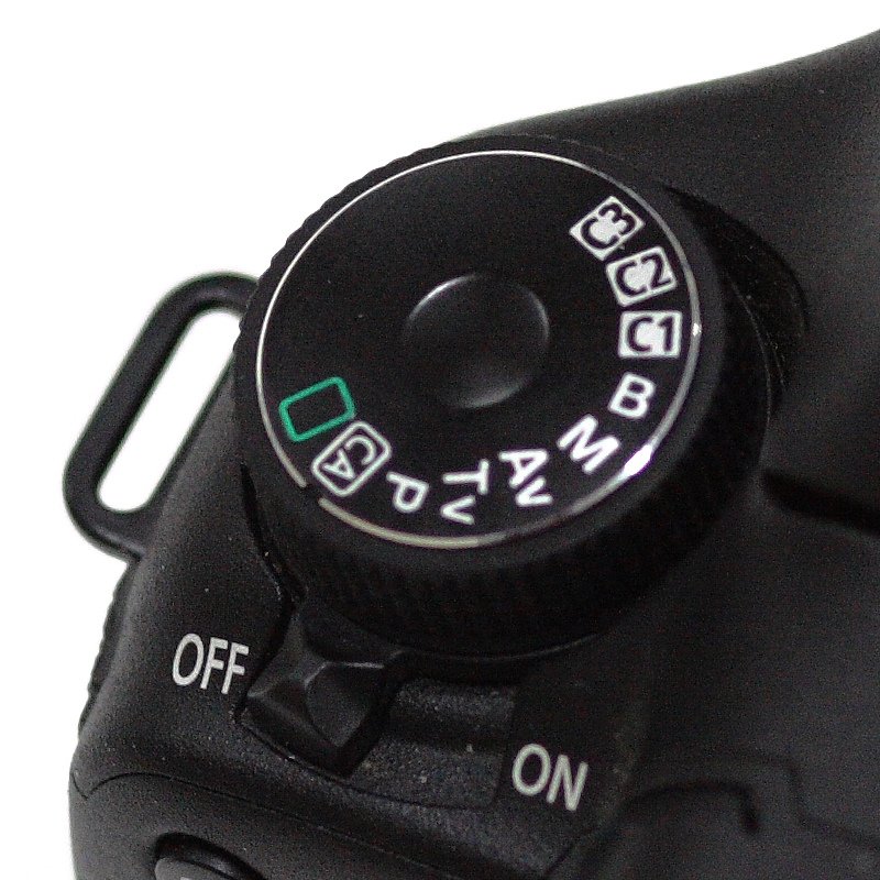 Top plate of a Canon DSLR showing the mode dial set to manual M, shutter wheel and ISO button, close-up detail for manual mode tutorial