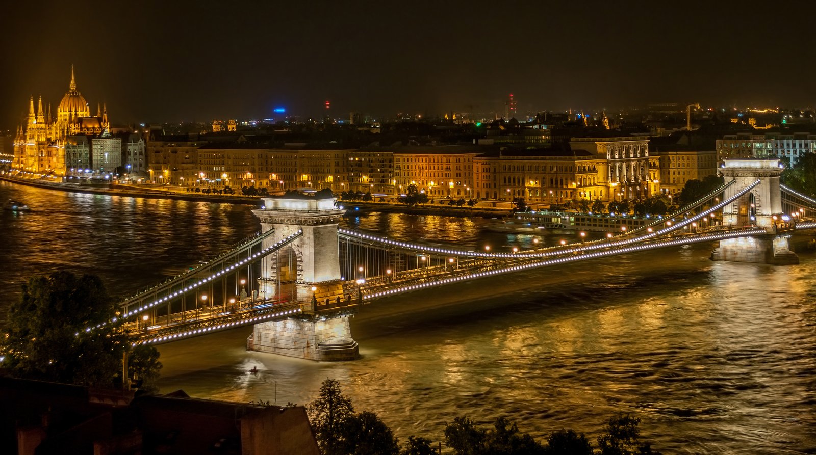Long exposure night cityscape of Szechenyi Chain Bridge over the Danube in Budapest, illuminated lights reflecting on water, low-light photography example