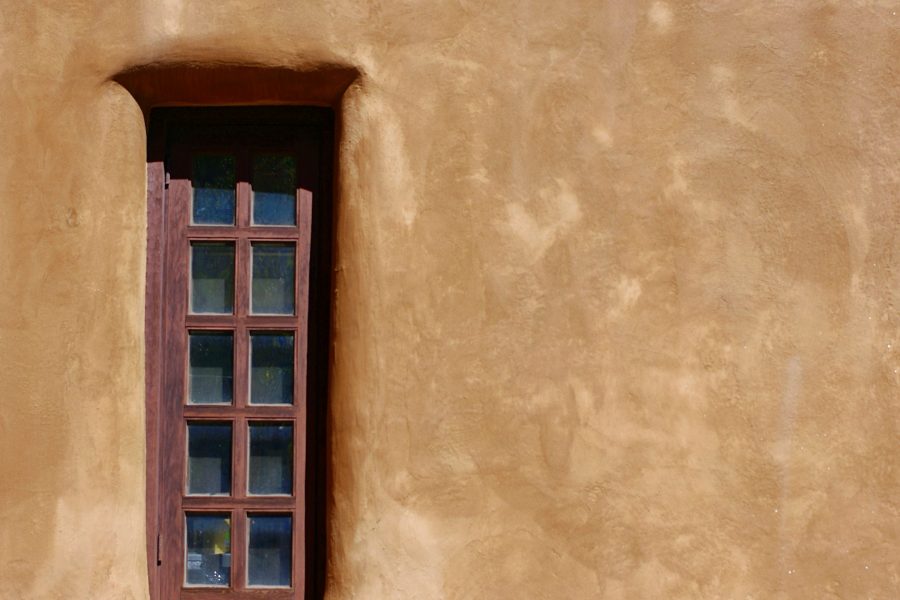 Wood-framed window and deep beam shadows on a warm adobe wall in Santa Fe, New Mexico.