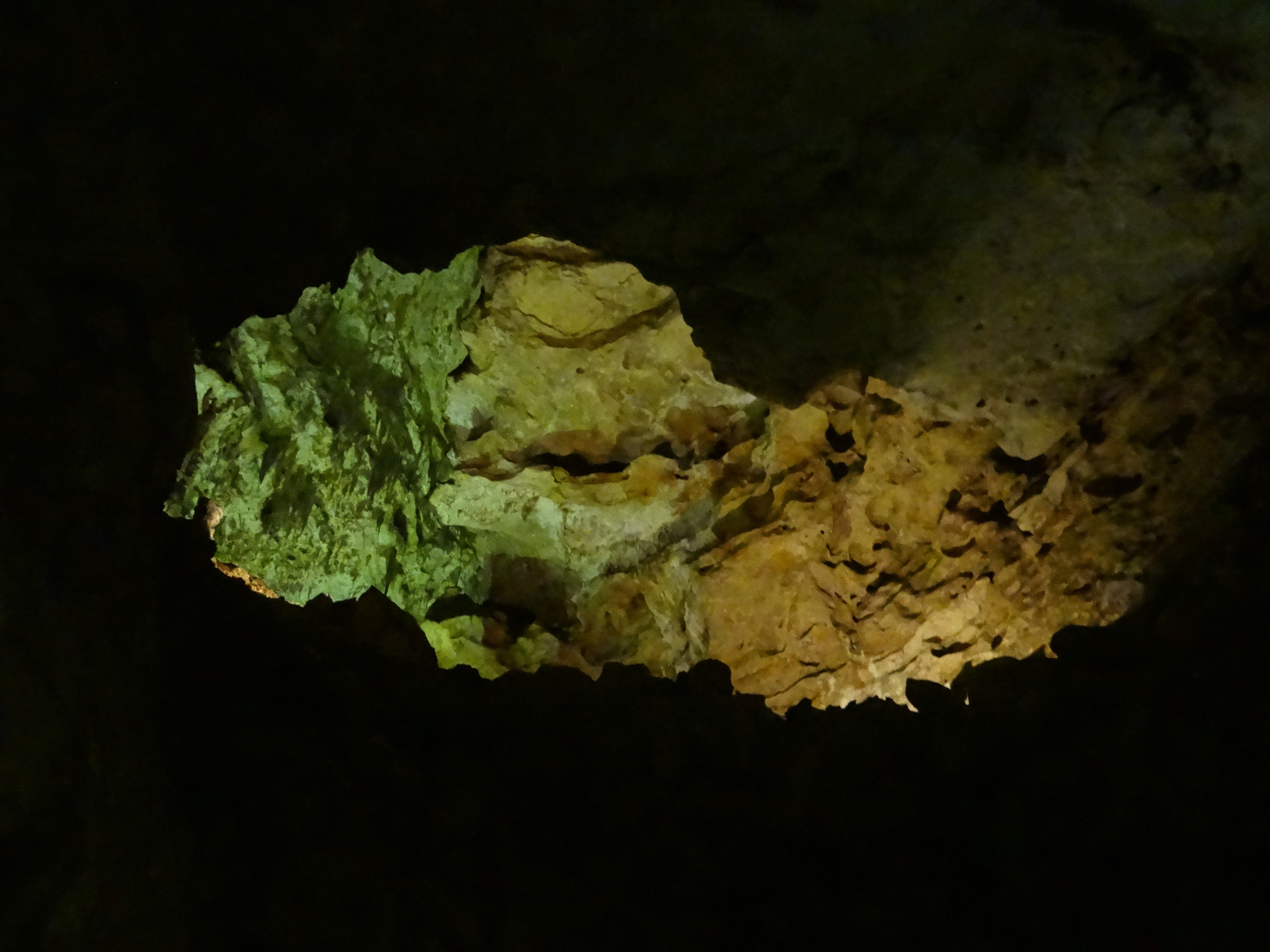 Green and warm light on a rock formation against a dark background in Carlsbad Caverns