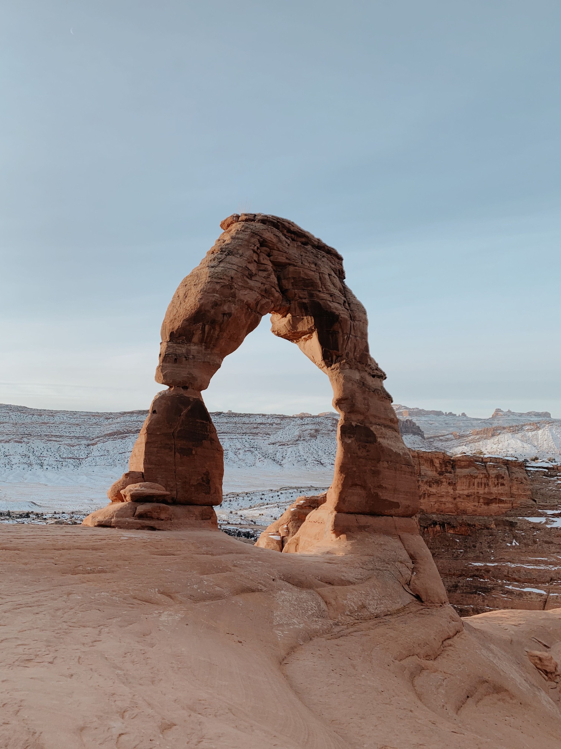 Delicate Arch above a winter landscape with snow on distant rock