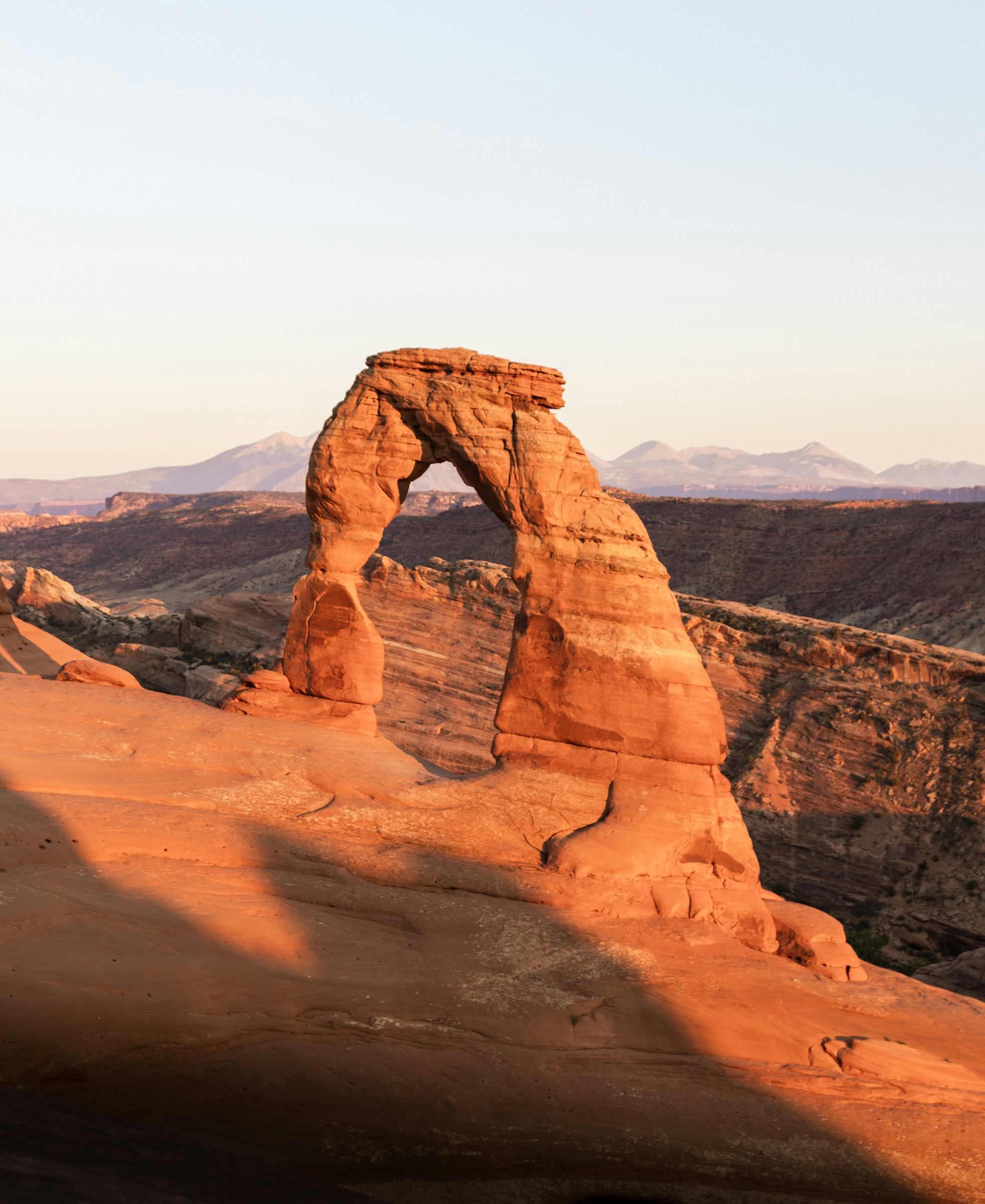 Delicate Arch in warm light with distant mountains behind the opening