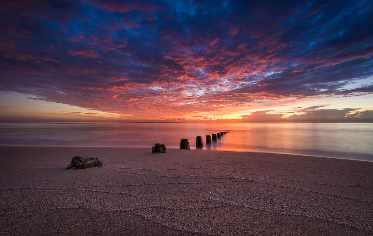 Wooden posts on a Miami beach beneath a colorful sunset