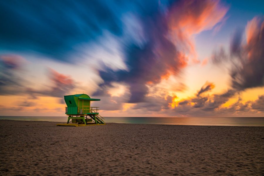 Green lifeguard tower beneath blue and orange sunset clouds